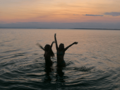 Image of two sillhouettes in a body of water against the sunset.
