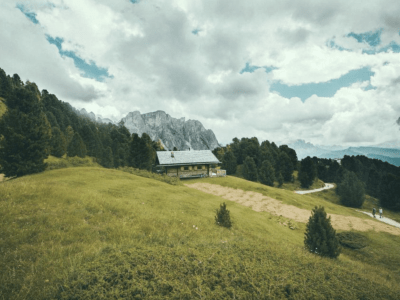 Image of a house situated on a rolling hillside with mountains in the background.