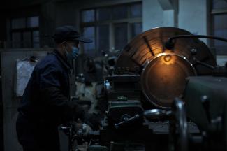 A factory worker in darkness operates a warmly lit machine. 