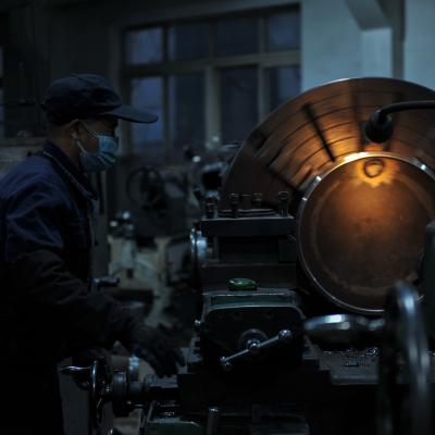 A factory worker in darkness operates a warmly lit machine. 