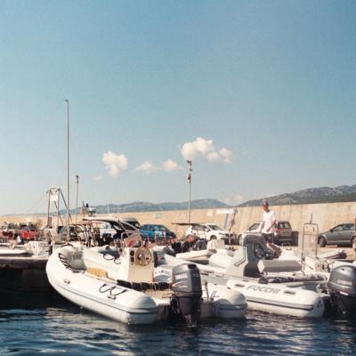 A photo of some dingys tied up to a dock in Italy with a little bit of the mountains and clouds in the background 