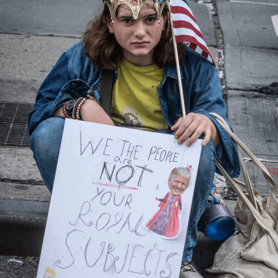 young protester with upside down crown and sign at No Kings protest